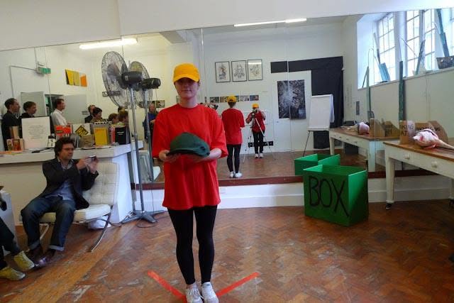 Sluice Art Fair — the performer holding a dark green cap with both hands before the audience