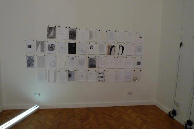 Sluice Art Fair — printed papers and sketches pinned to a gallery wall, with headphones and a light tube on the floor