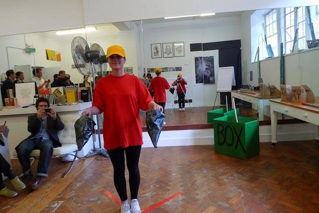 Sluice Art Fair — the performer holding two dark plastic bags before viewers and mirrored reflections