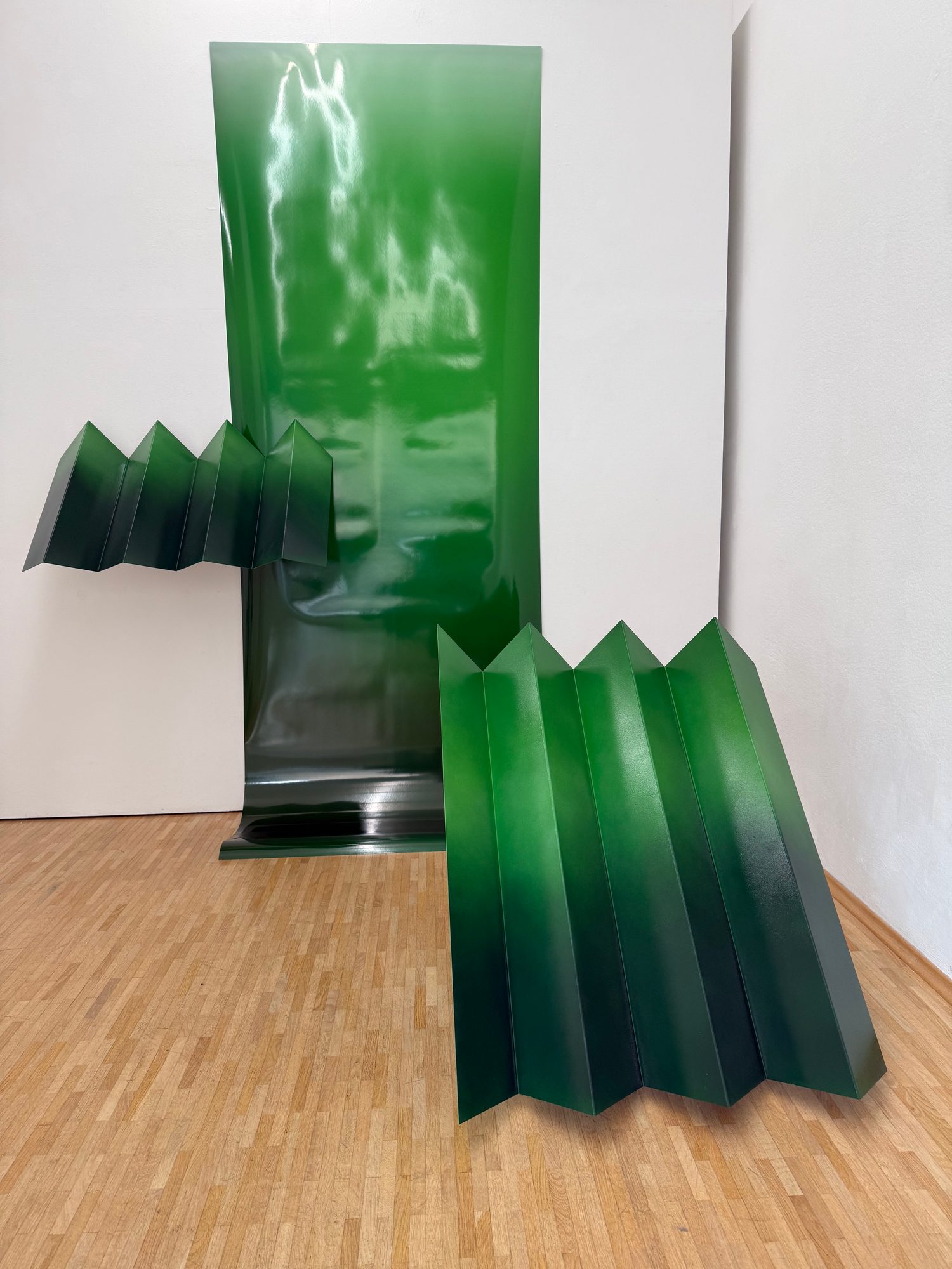 Folded green metal sculptures with a draped sheet