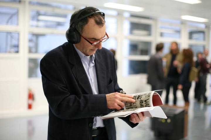 A visitor wearing headphones reads a booklet printed with the words AM, WAR and BEAR