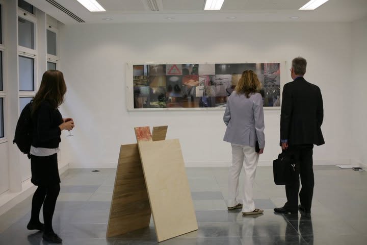Three visitors viewing a freestanding plywood sculpture and a large panoramic photo collage