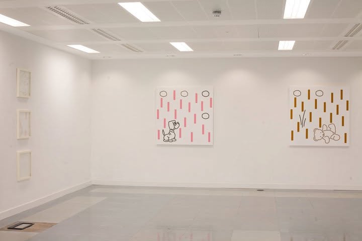 Two square paintings of a dog and a teddy bear on the gallery wall, with three small framed works alongside