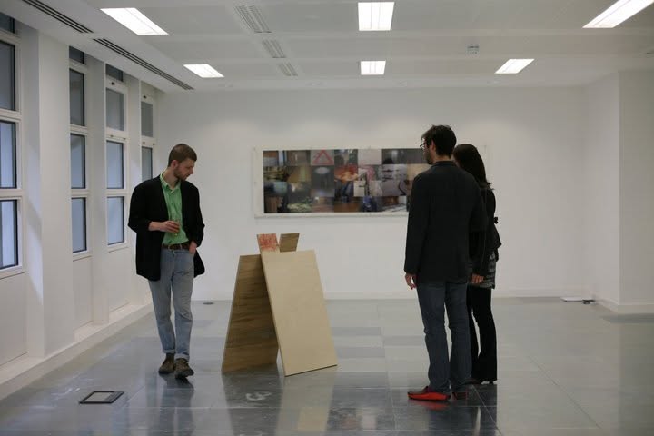 Visitors viewing a freestanding wooden panel sculpture and a panoramic photographic collage